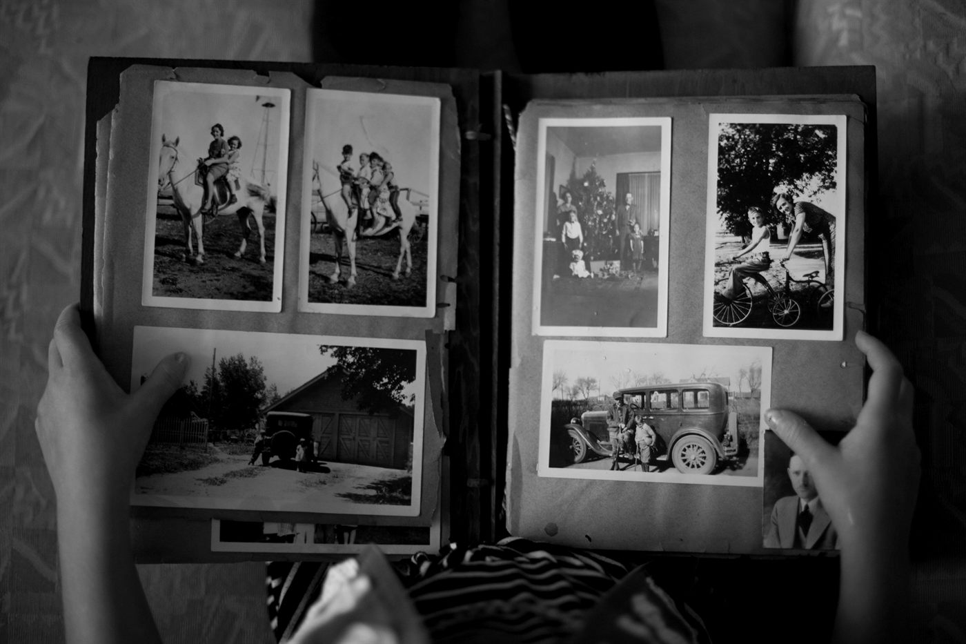 Hands holding open a family photo album of old black and white snapshots